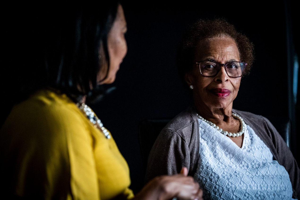 A photo of an older woman looking at the camera with her adult daughter next to her.