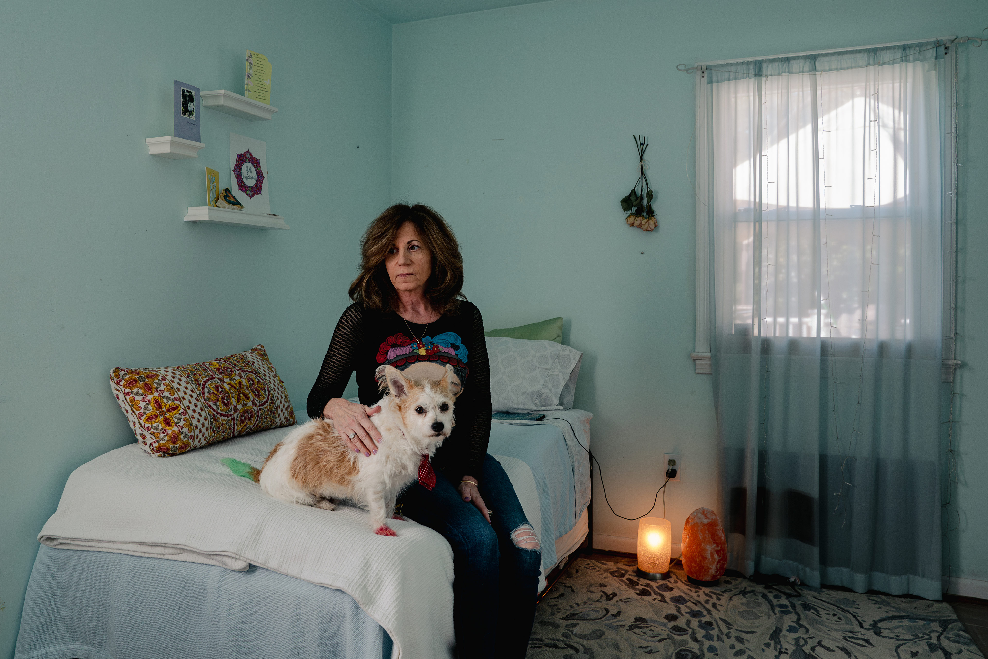 A photo of a woman sitting on a bed and petting a dog.