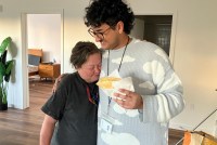 Julian Prado, a tall 29-year-old man with a nose piercing and black mustache, hugs Carla Brown while holding a taco in his other hand. Brown is a 60-year-old woman.