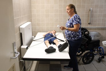 A photo of a woman making use of an adult-size changing table with her son in a restroom.