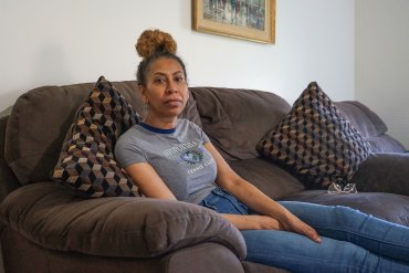 A woman in jeans and a t-shirt sits on a couch with her legs outstretched and looks at the camera.