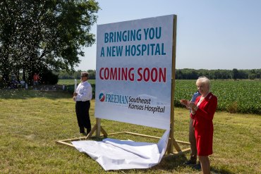 A photo of two people standing next to a sign that reads, "Bringing a new hospital to you. Coming soon."