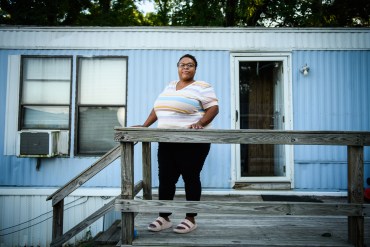 A photo of a woman standing in front of her blue mobile home.