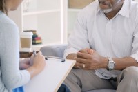 An unrecognizable mental health professional takes notes while sitting across from a patient.