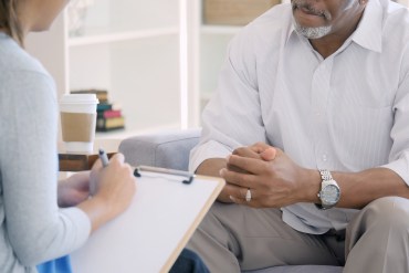 An unrecognizable mental health professional takes notes while sitting across from a patient.