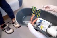 A photo of a nurse holding a container with two syringes and two bandages. A child is seen sitting from the waist down in the background.