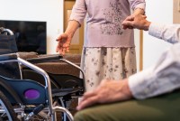 A woman helps a senior man into a wheelchair