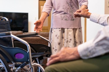 A woman helps a senior man into a wheelchair