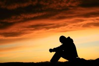 A silhouette of a young man sitting outside. Behind him is a vivid sunset.