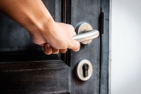 An up close shot of a hand turning a metal doorknob on a brown, wooden door.