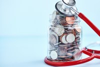 A jar filled with coins is wrapped with a red stethoscope.