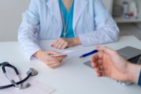 A patient handing a slip of paper to a doctor.