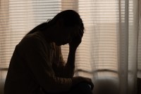 A silhouette of a figure sitting alone in a dark bedroom.