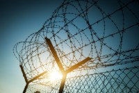 Sun shines through a barbed wire fence.