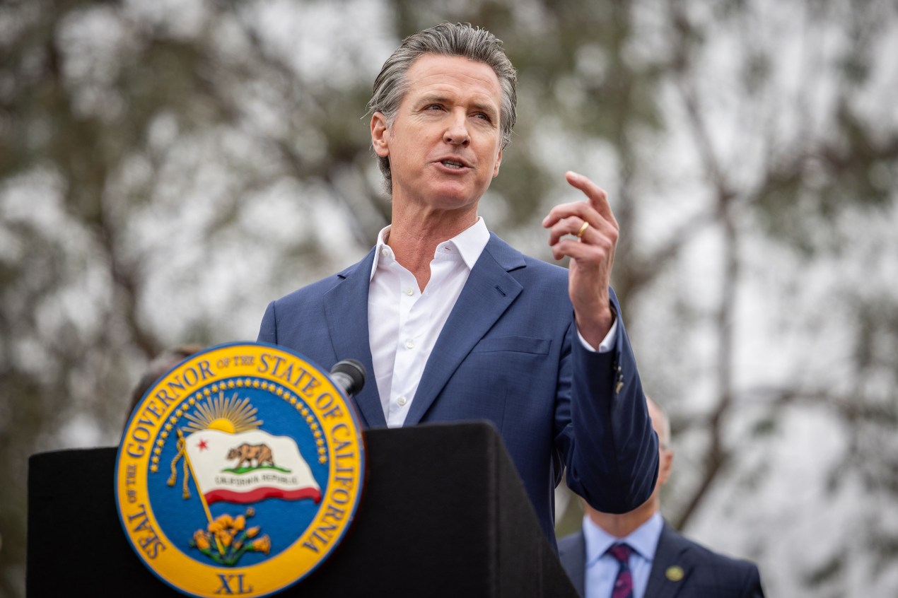 California Governor Gavin Newsom speaking at a podium outdoors.