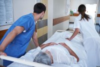 A photo of medical staff in a hospital wheeling an elder patient down a hallway on a gurney.