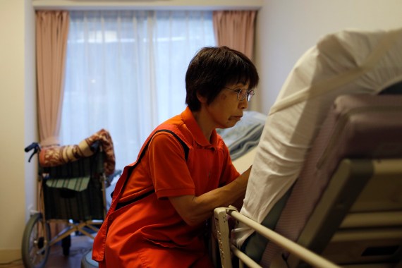 A photo of a female caregiver sitting next to a nursing home patient who is unidentifiable.