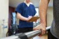 An unidentifiable patient is undergoing physical therapy while a health care professional takes notes behind them.