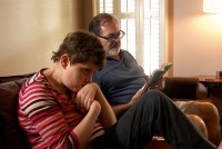 A photo of an older man reading on the couch in the background. His adult daughter, who is blind and has cerebral palsy, sits in the foreground.