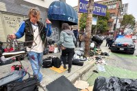 A photo of a pair of homeless people gathering their belongings as police officers watch.