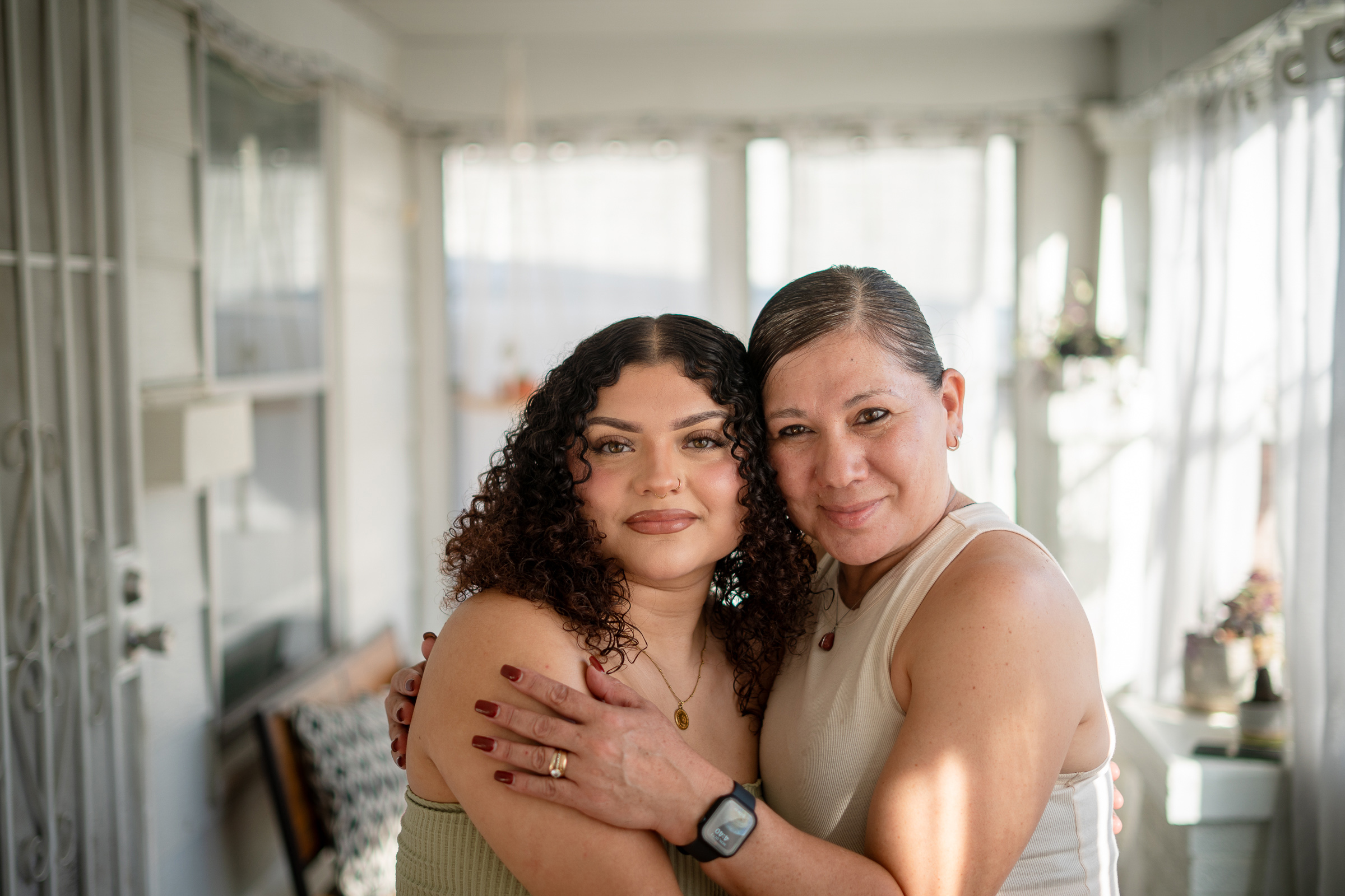 Two women pose for a photo with their arms wrapped around one another while looking at the camera