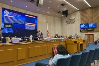 A court room with a large projector screen at the front. There are rows of blue chairs facing the screen.