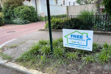 A sign on a lawn reads 'Free Lead Replacement'