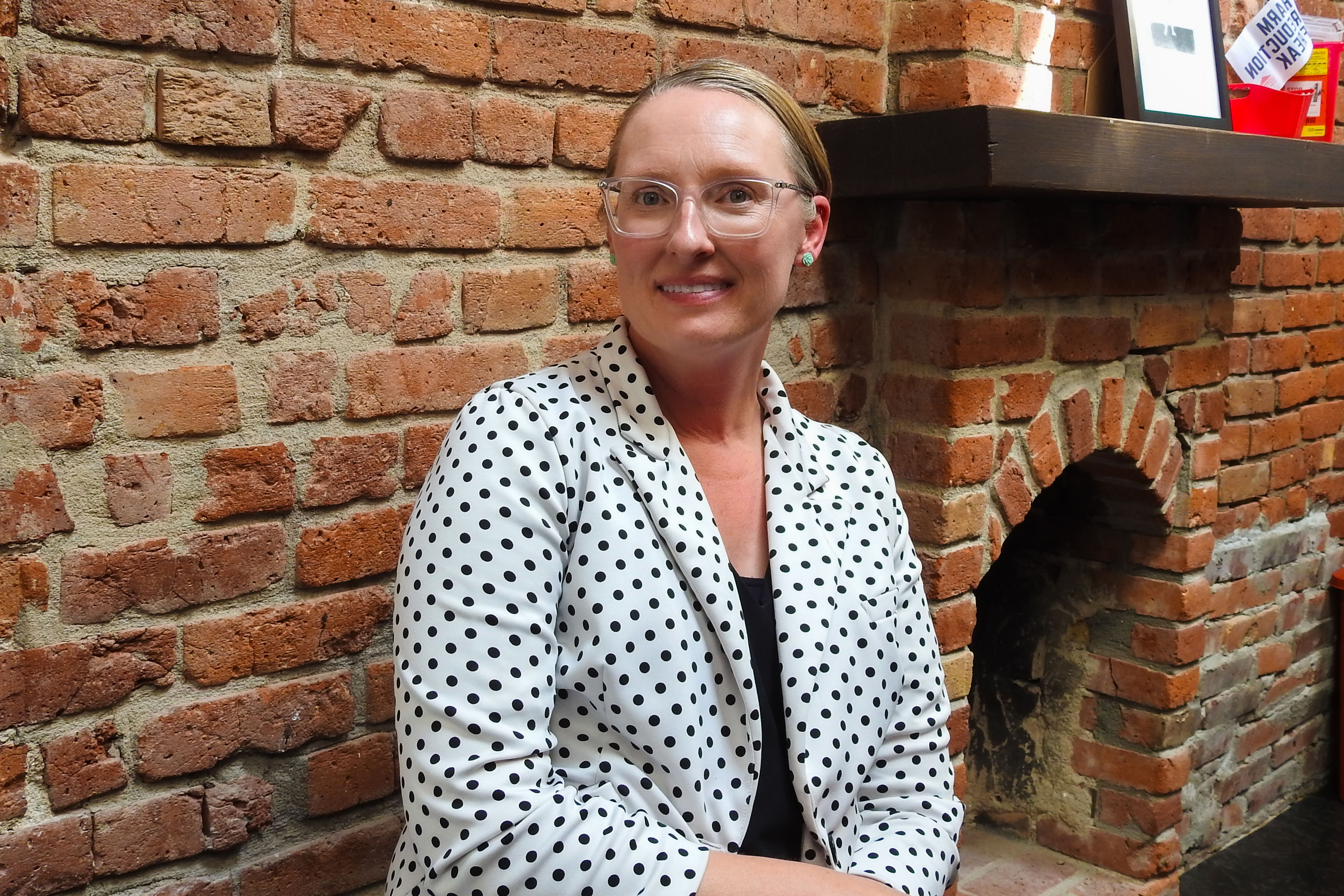 A portrait photograph of Lisa Raville. She wears a white blazer with black polka dots and wears glasses.