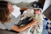 A woman with a black and white striped shirt sits in a chair and feeds a baby in a white pajama with a bottle