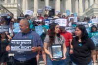 People of various ages and genders are standing in front of the U.S. Capitol building. Many hold signs that read, "Water Breaks = Basic Right". The female in the front of the line holds a framed photograph.