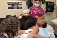 A photo of a young Black woman lying down as two medical workers assist her.